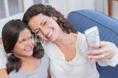 Happy mother and daughter sitting on the couch and taking selfie