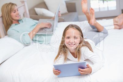 Mother using laptop while daughter using tablet pc on the bed