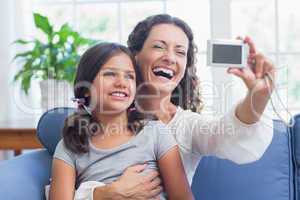 Happy mother and daughter sitting on the couch and taking selfie