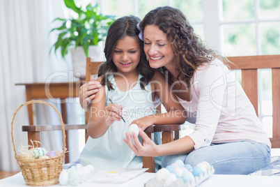 Happy mother and daughter painting easter eggs