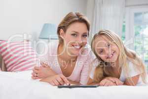 Mother and daughter using tablet together on bed