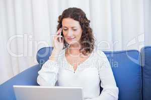 Pretty brunette speaking on the phone while using her laptop