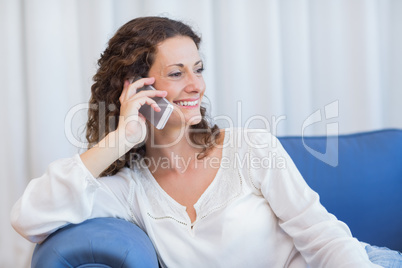 Smiling woman sitting on the couch and speaking on the phone