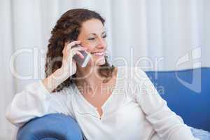 Smiling woman sitting on the couch and speaking on the phone