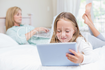 Mother using laptop while daughter using tablet pc on the bed Mother using laptop while daughter using tablet pc on the bed