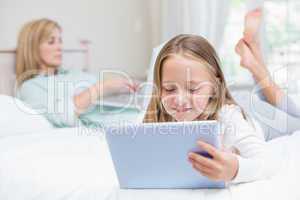 Mother using laptop while daughter using tablet pc on the bed