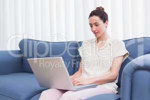 Casual brunette using laptop on couch