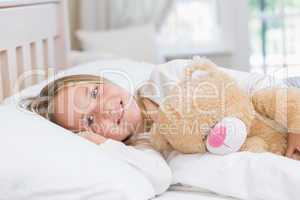 Little girl lying in her bed holding her teddy