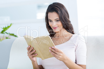 Smiling beautiful brunette relaxing and reading a book on the co