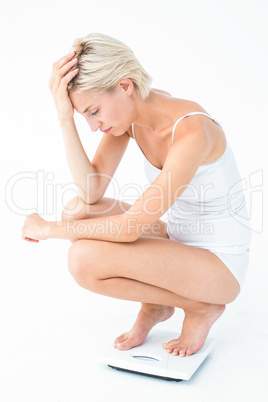 Sad woman squatting on scales
