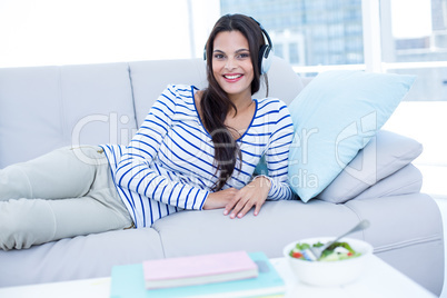 Smiling beautiful brunette relaxing on the couch and listening m