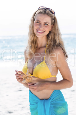 Smiling pretty blonde in bikini holding a starfish and looking a