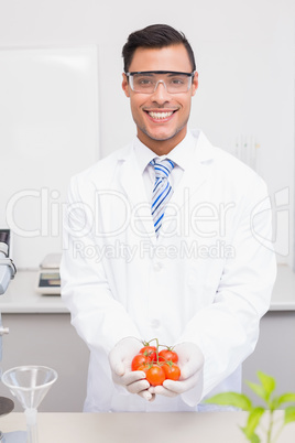Smiling scientist with protective glasses holding tomatoes