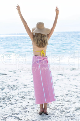 Happy blonde standing by the sea arms raised