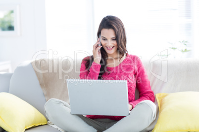 Smiling beautiful brunette speaking on the phone while using lap