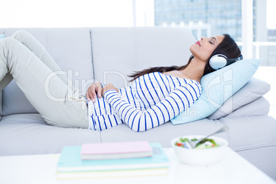 Smiling beautiful brunette relaxing on the couch and listening m