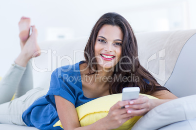 Smiling beautiful brunette relaxing on the couch and using her p