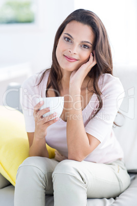 Smiling beautiful brunette relaxing on the couch and holding mug