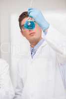 Scientist looking at beaker with blue fluid