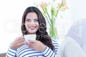 Smiling beautiful brunette relaxing on the couch and holding mug