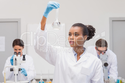 Scientist looking at white precipitate while colleagues working
