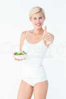 Beautiful fit woman holding a bowl of salad with thumbs up