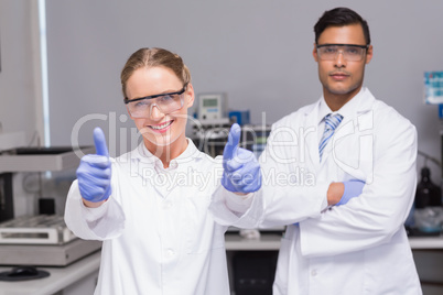 Smiling scientist looking at camera thumbs up with her colleague