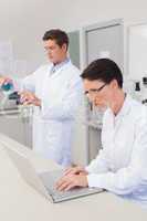 Scientist working attentively with laptop and another with beake