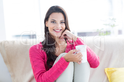 Smiling beautiful brunette relaxing on the couch and holding mug