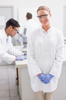 Smiling scientist looking at camera while colleagues working beh