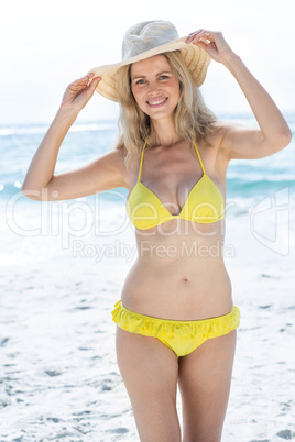 Smiling pretty blonde in bikini wearing straw hat and looking at