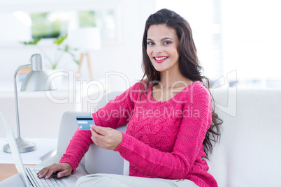 Smiling beautiful brunette doing online shopping on the couch