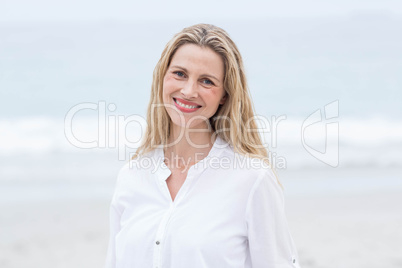 Smiling blonde standing by the sea and looking at camera