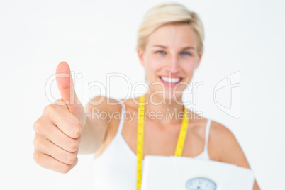 Happy woman holding scales with thumbs up