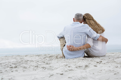 Happy couple sitting on the sand and looking at the sea