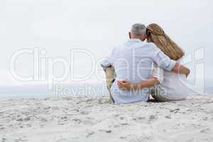 Happy couple sitting on the sand and looking at the sea