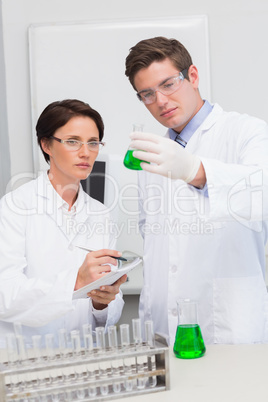 Scientists examining attentively beaker with green fluid