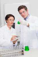 Scientists examining attentively beaker with green fluid