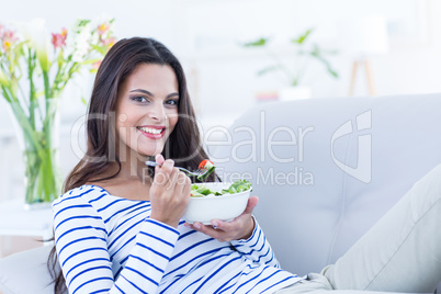 Smiling beautiful brunette relaxing on the couch and eating sala