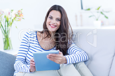 Smiling beautiful brunette relaxing on the couch and using her t