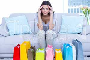Worried brunette sitting on the couch with shopping bags