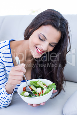 Smiling beautiful brunette relaxing on the couch and eating sala