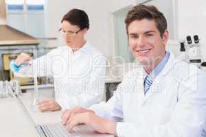 Scientist working attentively with laptop and another with beake