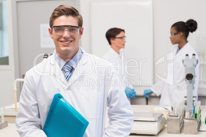 Scientist smiling at camera while colleagues talking together Scientist smiling at camera while colleagues talking together