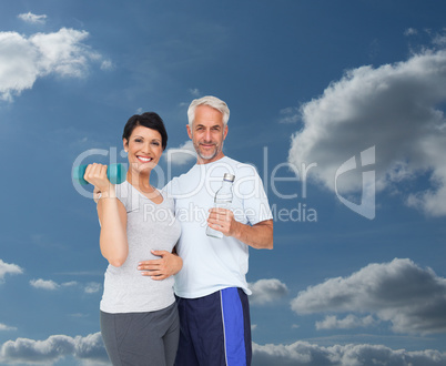 Composite image of happy fit couple with dumbbell and water bott