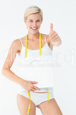 Happy woman holding scales with thumbs up