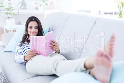 Smiling beautiful brunette relaxing on the couch and reading a b