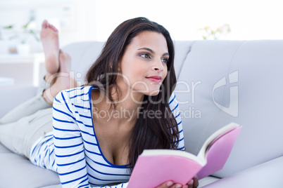 Smiling beautiful brunette relaxing on the couch and reading a b