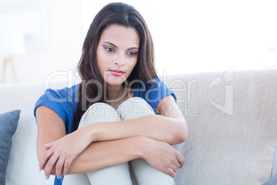 Thoughtful beautiful brunette sitting on the couch