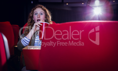 Young woman watching a film and drinking a soda